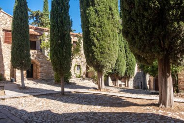 Yunanistan 'ın Chios Adası' ndaki Nea Moni 'de kırsal taş manastır binalarının yanındaki kaldırım taşı bahçesini uzun selvi ağaçları gölgeliyor