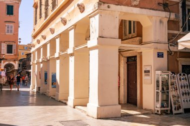 Korfu, Yunanistan, 4 Haziran 2025. Eski kasabadaki sokak manzarası, neoklasik sütunlar, pastel renkli binalar ve yaya geçidi boyunca yürüyen insanlar.