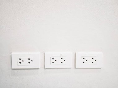 Beyaz beton duvarda üç beyaz elektrik prizi var.