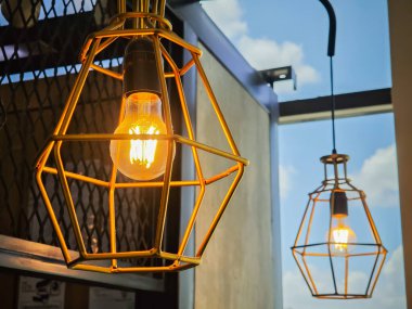 Geometrik altın kafes kolye lambasında klasik endüstriyel Edison ampulü.