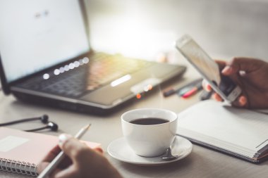 fincan kahve ve akıllı telefon iş adamı dizüstü bilgisayar ve yazma dizüstü kullanarak el ile