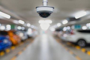 Bulanık araçları ve hafif ışıklandırması olan, halka açık alanlarda gözetim, izleme ve güvenliği temsil eden bir yeraltı otoparkına yerleştirilmiş modern CCTV kamera..