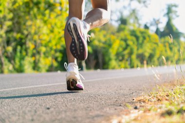 Çevresi yeşilliklerle çevrili boş asfalt yolda koşan bir sporcu. Spor eğitimi, kardiyo çalışması, özgürlük ve sağlıklı yaşam tarzı..
