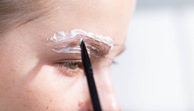 Genç kadın kaşlarını boyuyor, kaş kıllarını yakın plan yapıyor. Ev makyajı..