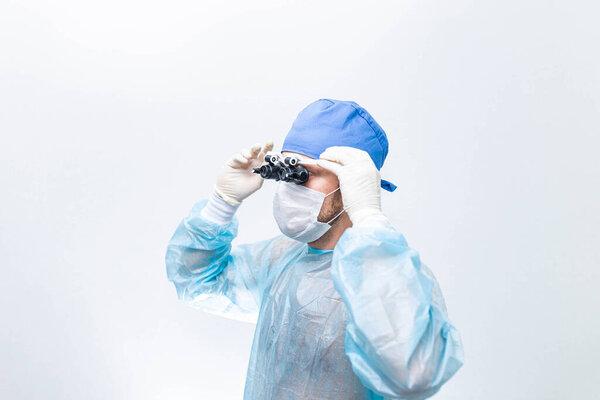 Мужской хирург в форме и микрохирургических очках на светлом фоне.