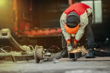Koruyucu miğferli bir erkek işçi, öğütücü ile metal keser, araba tamir eder..