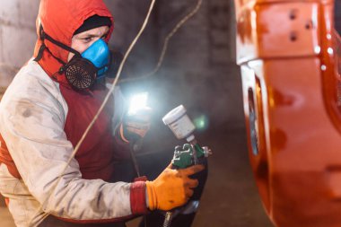 Solunum cihazındaki adam bir arabayı sprey boyayla kırmızıya boyuyor..