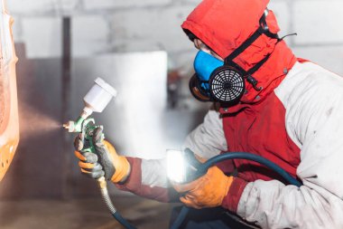 Solunum cihazındaki adam bir arabayı sprey boyayla kırmızıya boyuyor..