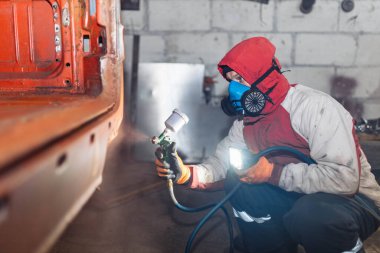 Solunum cihazındaki adam bir arabayı sprey boyayla kırmızıya boyuyor..