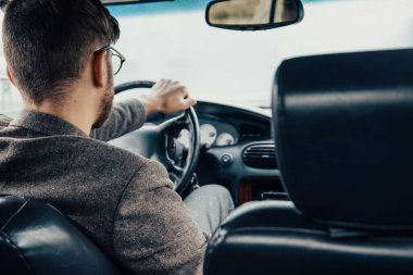 Gözlüklü ve ceketli bir erkek sürücü gün boyunca araba kullanıyor..