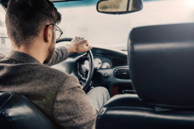 Gözlüklü ve ceketli bir erkek sürücü gün boyunca araba kullanıyor..