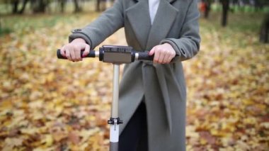 Sonbahar parkında elektrikli scooterlı bir kadın. Soğuk havada elektrikli aracın üstünde gitmek