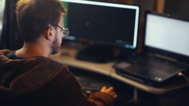 tired hacker in a black room working on computers with several screens