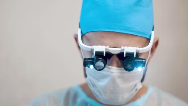 手術室で患者を手術する両眼拡大鏡を装着した外科医の映像です — ストック動画