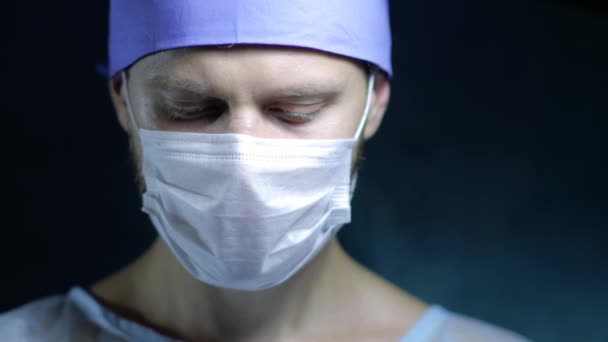 一个戴口罩的年轻外科医生认真地看着摄像机的镜头 — 图库视频影像