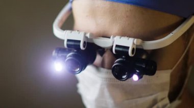 Karanlık bir ameliyathanede bir hastayı ameliyat ederken dürbün takan bir cerrahın görüntüleri.