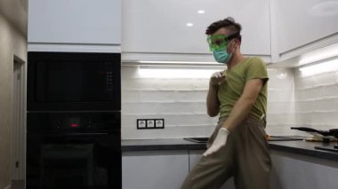 Tıbbi maskeli bir adam ve mutfakta gözlüklü bir adam dans edip oynaşıyor, kendini izole ediyor ve karantina altında..