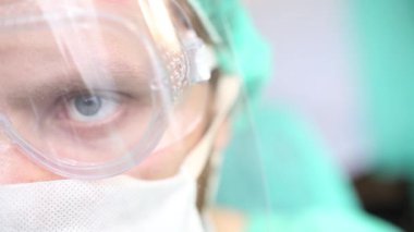 Ameliyathanede cerrah üniformalı, gözlüklü ve maskeli bir adam var..