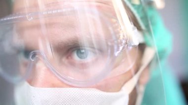 Ameliyathanede cerrah üniformalı, gözlüklü ve maskeli bir adam var..