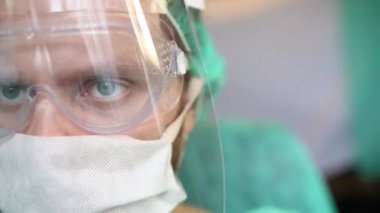 Ameliyathanede cerrah üniformalı, gözlüklü ve maskeli bir adam var..