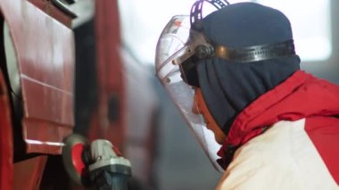 Koruyucu üniformalı ve kasklı bir adam fabrikada metal bir yüzeyi öğütüyor.