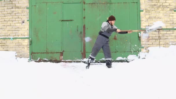 男性労働者は冬に工場のドアでシャベルで雪をきれいにし — ストック動画