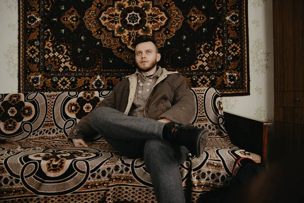 部屋に古いカーペットが敷かれたソファに座っている若い男の肖像画 — ストック写真