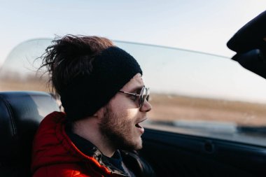Üstü açık bir arabayla gezen güneş gözlüklü bir adam.  