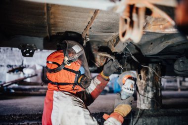 Araba kaportası işi, usta kamyonun altını öğütücüyle temizliyor.