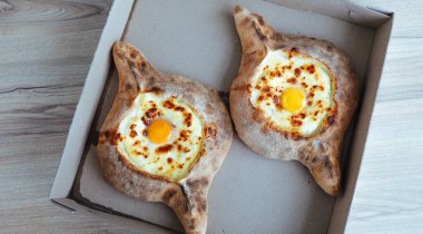Khachapuri karton bir kutuda Adjara 'da yumurtalı ve peynirli iştah açıcı bir yemek getiriyor.