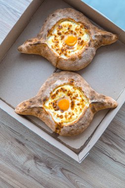 Khachapuri karton bir kutuda Adjara 'da yumurtalı ve peynirli iştah açıcı bir yemek getiriyor.