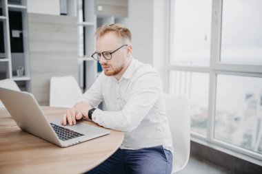 Avrupalı adam masada oturuyor ve dizüstü bilgisayarla çalışıyor, evde programlama yapıyor. Serbest İşçi çevrimiçi.