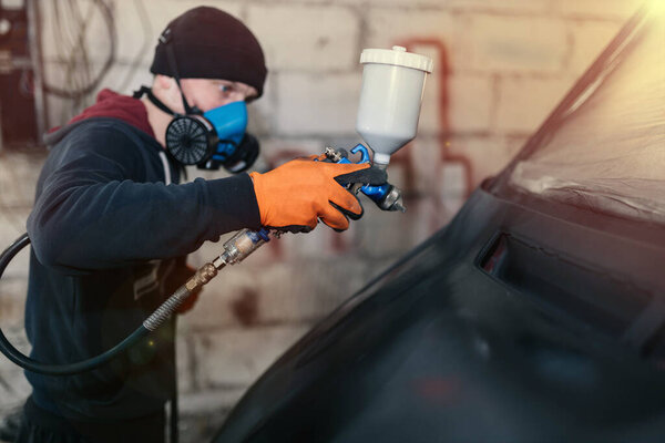 man paints a car, treatment of the body with epoxy primer.