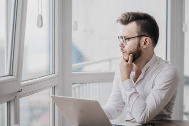 Gözlüklü sakallı adam evinde dizüstü bilgisayarıyla oturuyor ve çalışıyor, internetteki kişisel tecrit konsepti..