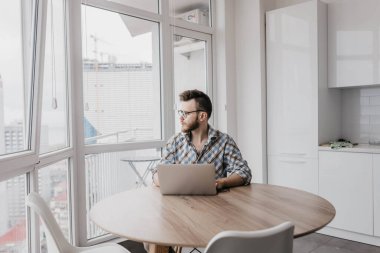 Gözlüklü sakallı adam evinde dizüstü bilgisayarıyla oturuyor ve çalışıyor, internetteki kişisel tecrit konsepti..
