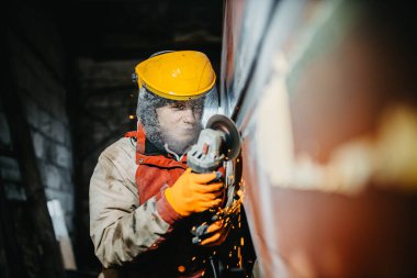 Erkek fabrika işçisi metal kaynaklarını öğütücüyle öğütüyor..