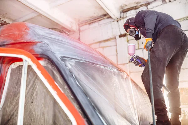 man in a home workshop paints a truck red with a spray bottle