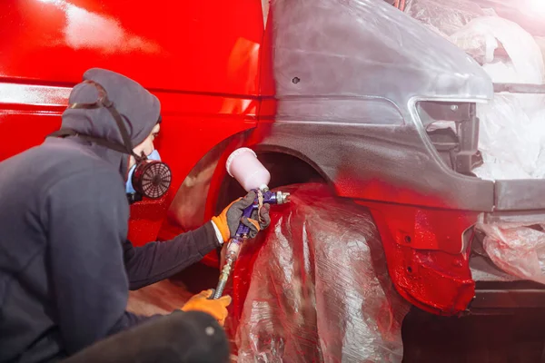 man in a home workshop paints a truck red with a spray bottle