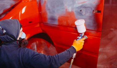 Atölyede çalışan bir adam bir kamyonu sprey boyayla kırmızıya boyuyor.