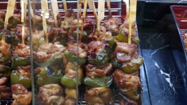 Yakından çekilmiş bir videoda, ağzı sulandıran yakitori tavuk şişleri ve yeşil biberler sergileniyor. Satıcı bu lezzetli yemeği hazırlarken aromatik tatlara ve mutfak sanatına tanık olun..