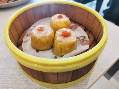 Geleneksel bambu buharlı sepetinde servis edilen lezzetli Çin Siu Mai hamur köftelerinin yakın çekimi, yemek pişirme deneyimini cezbediyor.