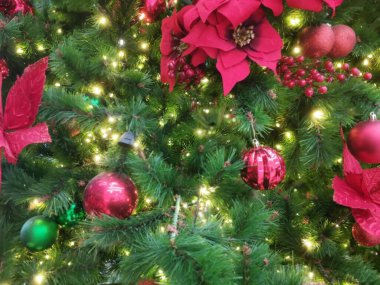 Kırmızı süslemelerle kaplı ışıldayan bir Noel ağacı ve altın ışıklarla parıldayan noktalar, tatil atmosferinin neşesini, rahatlığını ve parıltısını anımsatıyor..