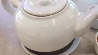 Rafine bir çay servisi videosu, iki fincan aromatik çayın yanında beyaz porselen bir çaydanlık sunar. Seyircileri sakin bir rahatlama ve refah anının tadını çıkarmaya davet eder..