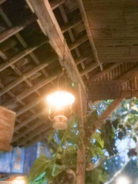 Yeşilliklerle çevrili, bambu ve ahşap çatının altında sıcacık parlayan rahat bir fener.