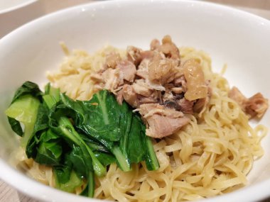 Lezzetli bir şehriye tabağı dilimlenmiş tavuk ve yapraklı yeşilliklerle kaplı, ahşap masada servis edilen bir kasede.