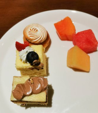 Kremalı turta, kremalı ve çikolatalı kekler ve taze meyve küpleri içeren renkli bir tatlı tabağı, çeşitli ve zarif bir açık büfe tarzı sunum.