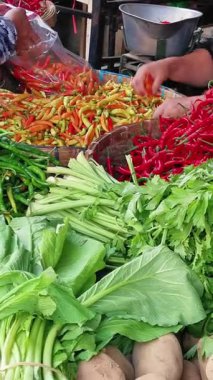 Geleneksel bir pazarda renkli kırmızı biberleri ve taze yapraklı sebzeleri kapayın. Bu arada satıcılar el yapımı ürünleri ayırıp seçiyorlar..