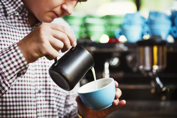 Man häller varm mjölk i en kopp kaffe — Stockfoto