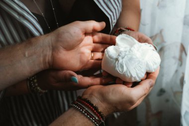Hands of two persons gently holding white baby shoes, representing anticipation and joy of expecting a child. This intimate moment captures love and family bonding