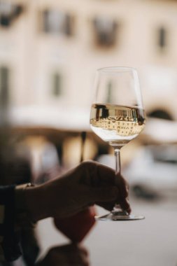 A hand holds a wine glass, capturing the reflection of a cityscape in the liquid. The scene suggests a leisurely moment, with blurred surroundings enhancing focus on the glass.